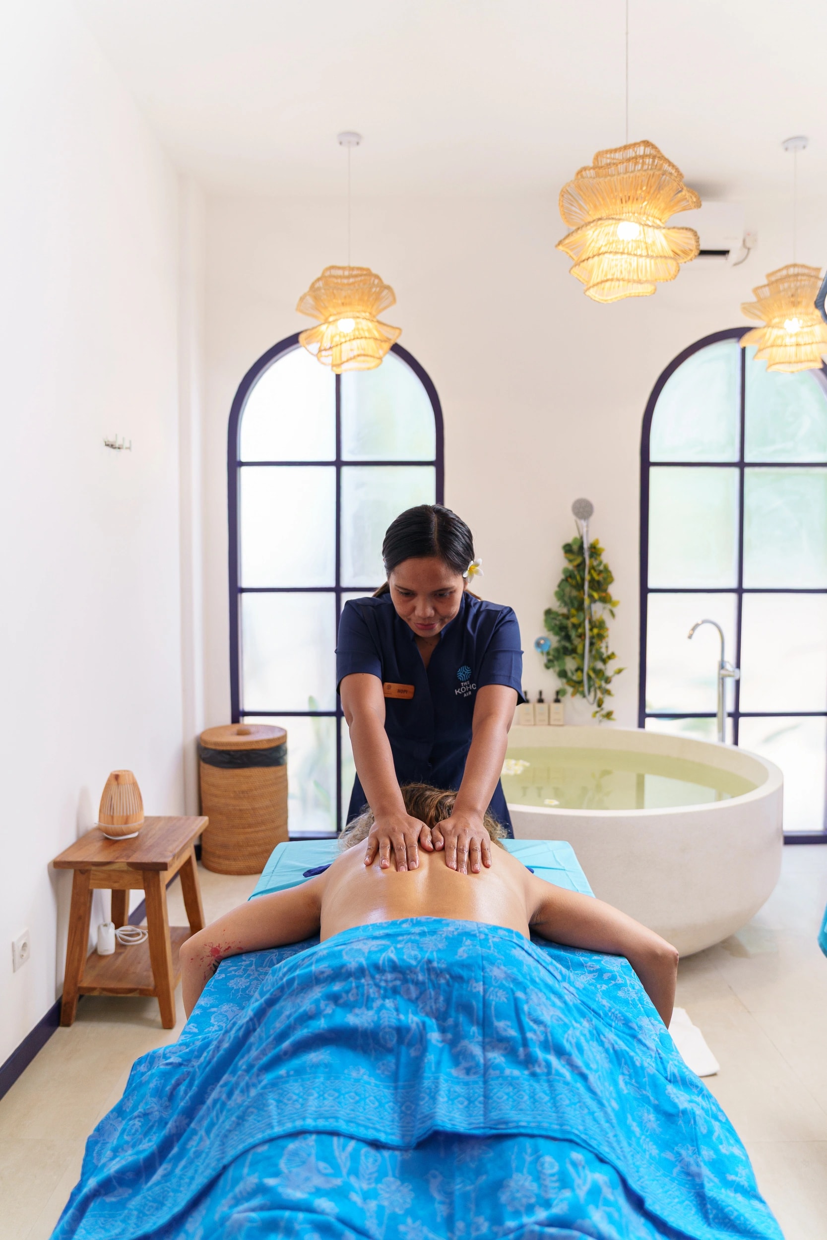 A masseuse giving a back massage to a guest lying on a treatment bed in a modern spa room.